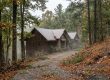 Cozy wooden cabin in a misty autumn forest, with a gravel path winding past fallen leaves.