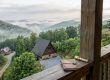 Notebook and brass telescope rest on a weathered wooden railing, overlooking a misty forested valley with cabins below in Highlands, NC.