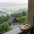 Notebook and brass telescope rest on a weathered wooden railing, overlooking a misty forested valley with cabins below in Highlands, NC.