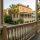 Wide porch of a historic beige house with white columns, palm trees, and a cobblestone street.