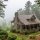 Cozy stone-and-wood cabin in a misty forest, with a wraparound porch and warm lights on. (informative image)