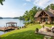 Lakeside house with stone and wood exterior, a spacious stone patio, and a wooden dock extending into a calm lake.