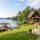 Lakeside house with stone and wood exterior, a spacious stone patio, and a wooden dock extending into a calm lake.