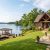 Lakeside house with stone and wood exterior, a spacious stone patio, and a wooden dock extending into a calm lake.