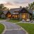 Luxurious stone-and-wood house with warm lighting, outdoor seating around a fire pit on a manicured lawn. Pre-arrival home prep
