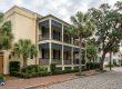 Three-story beige townhouse with blue shutters and wraparound balconies on a palm-lined street