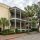 Three-story beige townhouse with blue shutters and wraparound balconies on a palm-lined street