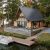 A-frame wooden cabin on a lakeside lot with a large deck, dock, and a boat beside calm water, surrounded by trees.