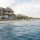 Large coastal house with wraparound porch on a sandy beach, people gathered on the patio.