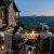 Couple sitting in Adirondack chairs around a stone fireplace on a patio, watching a sunset over rolling mountains.