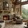 Cozy living room with a stone fireplace and large window showing a forested mountain view, leather pillows on soft chairs.