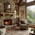 Cozy living room with a stone fireplace and large window showing a forested mountain view, leather pillows on soft chairs.
