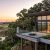 Sunset view from a modern house deck overlooking marshlands; a woman stands by a fire pit near a telescope.