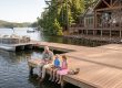 A man and two children fishing on a wooden dock by a lake, with a pontoon boat tied to the dock and a lakeside house in the background. Estate Maintenance Services