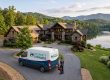 Luxurious stone home on a hill overlooking a lake and forest, with a Property Stewards van in the driveway.