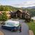 Luxurious stone home on a hill overlooking a lake and forest, with a Property Stewards van in the driveway.