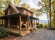 Man on a ladder repairs the roof of a wooden cabin surrounded by autumn trees on a spacious porch.