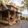 Man on a ladder repairs the roof of a wooden cabin surrounded by autumn trees on a spacious porch.