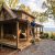 Man on a ladder repairs the roof of a wooden cabin surrounded by autumn trees on a spacious porch.