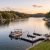 Pontoon boat with people on a calm lake at sunset, with shoreline homes and a wooden dock nearby.