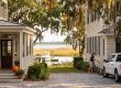 Front yard between two white houses with pumpkins on steps, leading to a marina and a docked boat in the distance by calm water.