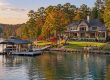 Lakeside luxury home with a dock, boat, and autumn trees along the shore.