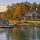 Lakeside luxury home with a dock, boat, and autumn trees along the shore.