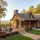 Cozy wooden mountain cabin with a large deck and stone columns, autumn trees surround the house, and a car in the driveway.
