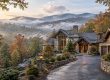 Luxurious stone mansion in autumn with misty valley and mountains in the background, lit driveway leading to the entrance