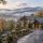 Luxurious stone mansion in autumn with misty valley and mountains in the background, lit driveway leading to the entrance