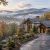 Luxurious stone mansion in autumn with misty valley and mountains in the background, lit driveway leading to the entrance